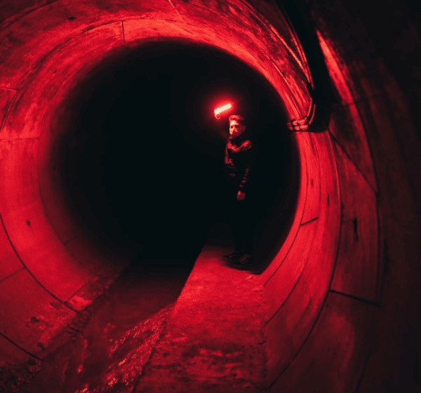 Man holding a red light inside a long drainage tunnel, representing the power of a 100ft drain snake for clearing stubborn blockages.
