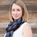 Kellie, a stylish mom and founder of The Yuppie Files lifestyle blog, wearing a plaid scarf and white top, smiling against a wooden background.