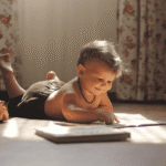 Smiling toddler lying on the floor and pointing at a book, symbolizing early learning and positive behavior support.