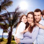 Smiling parents with their two children enjoying a sunny day at the beach with palm trees in the background.
