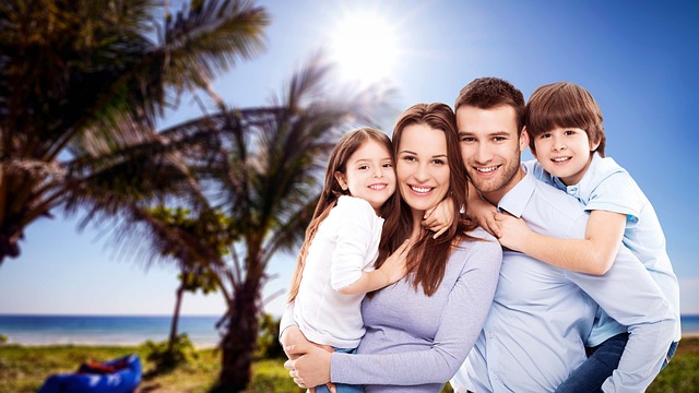 Smiling parents with their two children enjoying a sunny day at the beach with palm trees in the background.