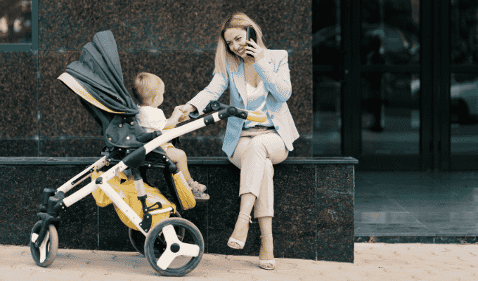 A mother sitting outdoors with her baby in a stroller, highlighting everyday considerations when choosing a baby’s first stroller.
