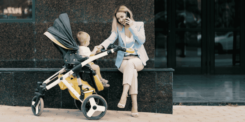 A mother sitting outdoors with her baby in a stroller, highlighting everyday considerations when choosing a baby’s first stroller.