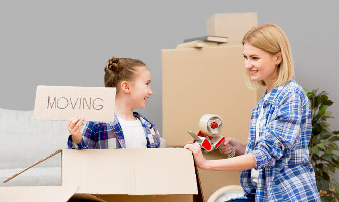 Mother and child packing boxes together, with the child holding a “moving” sign, illustrating a positive and calm approach to discussing relocation with kids.