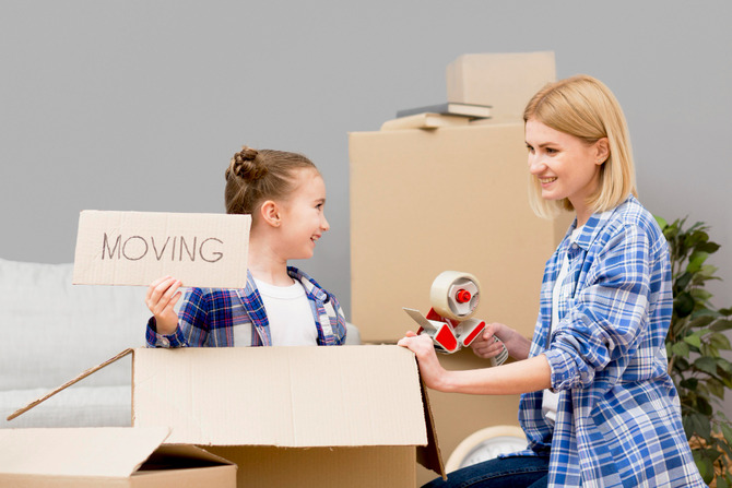 Mother and child packing boxes together, with the child holding a “moving” sign, illustrating a positive and calm approach to discussing relocation with kids.
