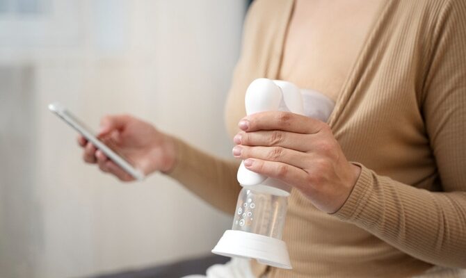 Mother using a portable breast pump while holding a smartphone, reflecting the convenience and mobility of modern motherhood.