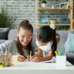 Mother helping her daughter with writing and learning activities at home, encouraging positive study habits and focused learning routines.