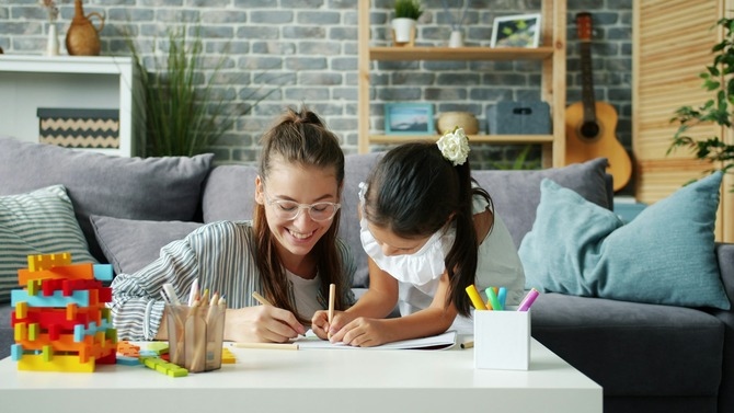 Mother helping her daughter with writing and learning activities at home, encouraging positive study habits and focused learning routines.