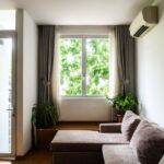 Living room with a cozy sofa, indoor plants, and a large window with curtains.
